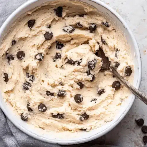 Top-down view of creamy chocolate chip cottage cheese cookie dough in a white bowl with a vintage spoon.
