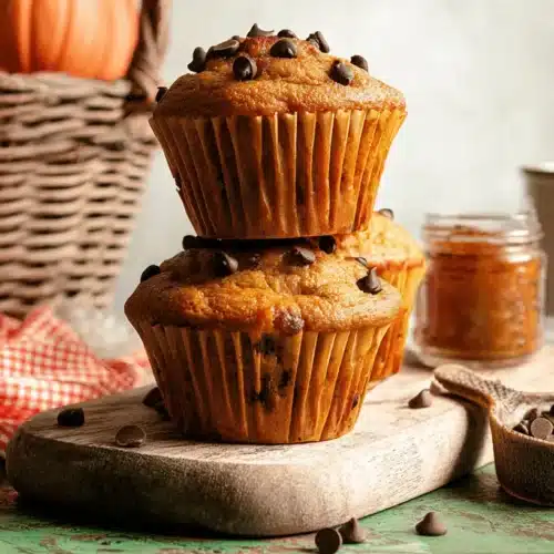 The Best Cottage Cheese Pumpkin Muffins 3 Stack of moist cottage cheese pumpkin muffins with chocolate chips on a rustic wooden board.