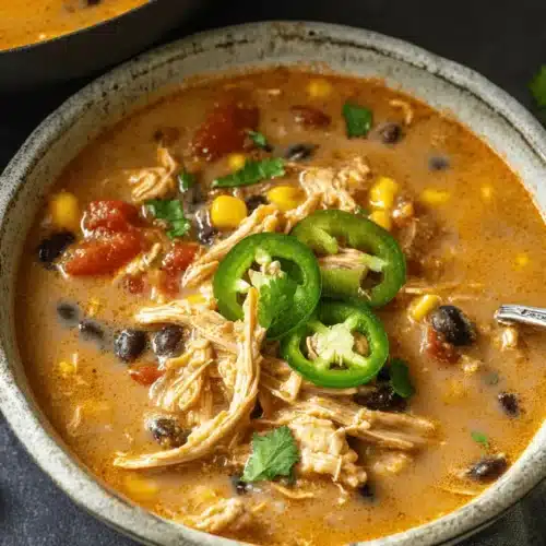 A rustic ceramic bowl overflowing with vibrant creamy chicken taco soup, garnished with fresh jalapeño slices and cilantro.