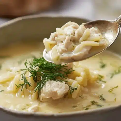 Authentic Avgolemono Soup: Creamy Greek Lemon Chicken with Orzo 2 Spoon scooping creamy avgolemono soup with chicken, orzo, and fresh dill.