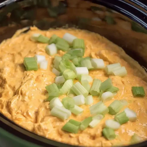 Warm, creamy buffalo chicken dip crock pot, garnished with fresh green onions and celery.