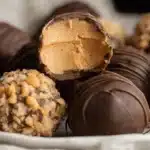 Close-up of homemade chocolate Butterfinger Balls with creamy peanut butter filling and various toppings on a white plate.