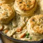 Warm chicken pot pie with biscuits, featuring golden, flaky biscuit tops and a creamy filling in a cast-iron skillet.