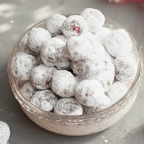 Festive cranberry candy, dusted with powdered sugar, in a bowl with red ribbons and glitter.