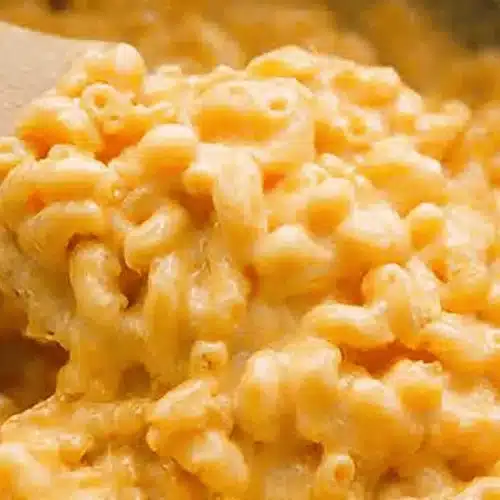 Close-up of creamy, delicious crockpot mac and cheese being served with a wooden spoon.