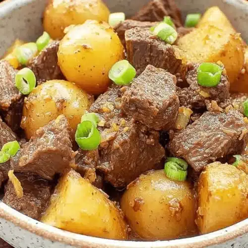 Close-up of savory crockpot steak bites with tender potatoes and fresh green onions in a rustic bowl.