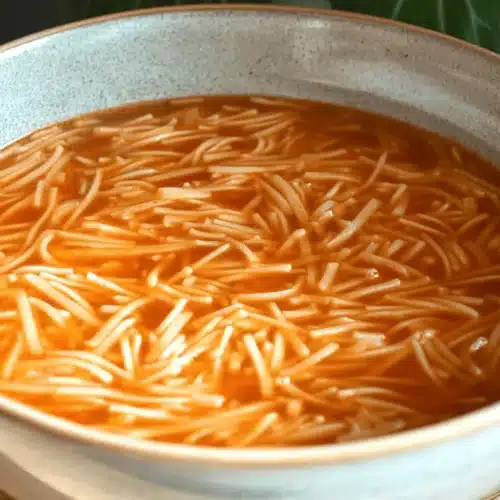 Easy Sopa de Fideo (Mexican Noodle Soup) 2 Close-up of a comforting bowl of fideo soup with thin noodles in a vibrant reddish-orange broth.