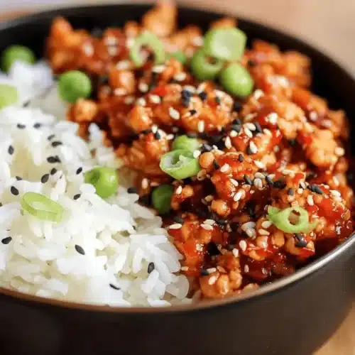 Close-up of two appetizing bowls of Firecracker Ground Chicken served with white rice, sesame seeds, and green onions.