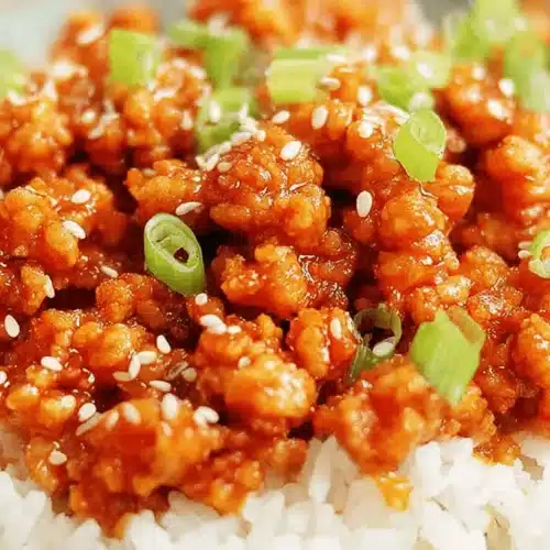 A close-up of a bowl of delicious Ground Orange Chicken served over fluffy white rice, garnished with fresh green onions and sesame seeds.