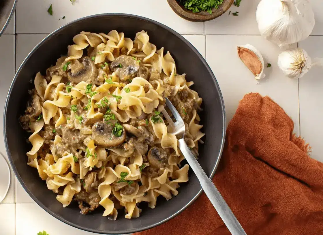 High-Protein Beef Stroganoff: A Healthier Twist on a Classic 1 Overhead view of a hearty High-Protein Beef Stroganoff with wavy egg noodles, mushrooms, and fresh parsley, served in dark bowls.