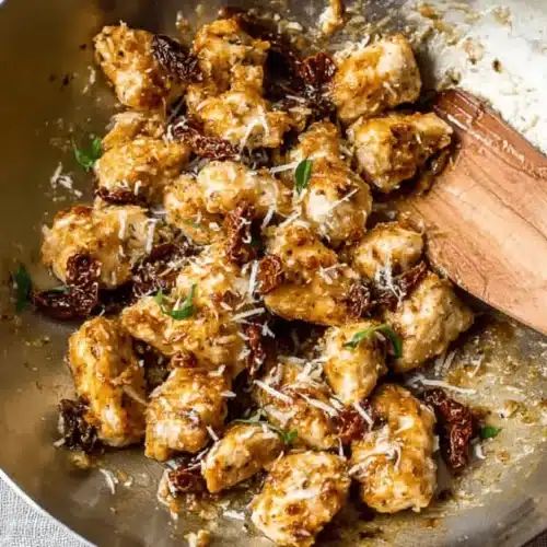 A rustic skillet overflowing with golden-brown Marry Me Chicken Bites, featuring sun-dried tomatoes, grated Parmesan, and fresh herbs, ready to be served.