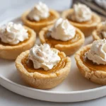 Close-up of delicious Mini Pumpkin Pies with whipped cream on a white platter, perfect for autumn desserts.