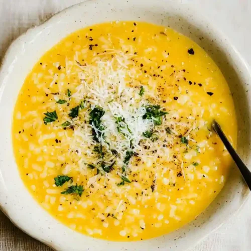 A close-up of a warm, golden-yellow penicillin soup with orzo, grated cheese, and fresh herbs in a rustic ceramic bowl.