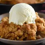 Close-up of a warm Pumpkin Pie Crisp with a scoop of melting vanilla ice cream in a rustic bowl.