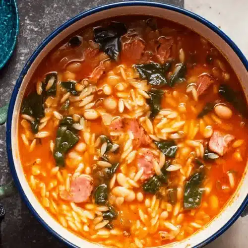 Hearty Southern Swamp Soup Recipe 2 A vibrant swamp soup recipe in an enameled pot, brimming with pasta, beans, and leafy greens, served with golden spoons.