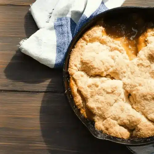 Southern Comfort: The Best Sweet Potato Cobbler Recipe 2 Warm sweet potato cobbler in a cast-iron skillet on a rustic wooden surface.