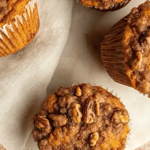 Four golden sweet potato muffins with pecan streusel topping, artfully arranged on rustic surfaces, ideal for a sweet potato muffin recipe.
