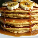 Caramel Banana Protein Pancakes stacked with sliced bananas and caramel drizzle on a white plate.