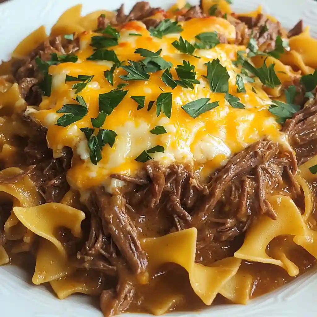Creamy beef and noodles topped with melted cheese and fresh parsley on a white plate