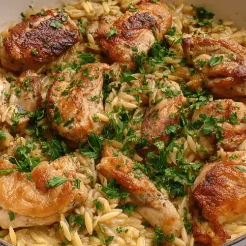 Close-up of creamy chicken orzo pasta garnished with fresh herbs in a white cast-iron pan.