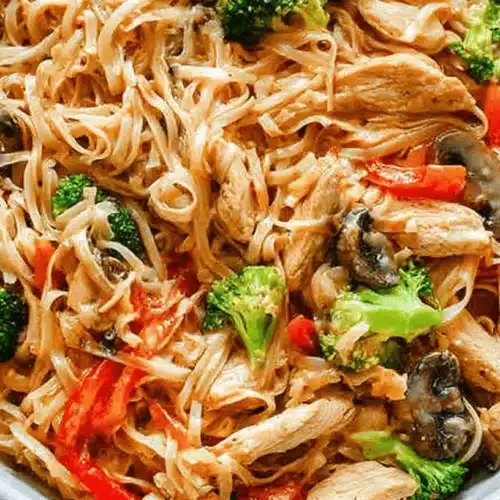 Vibrant close-up of a large bowl of chicken stir fry with noodles, featuring chicken, broccoli, red bell pepper, and mushrooms.