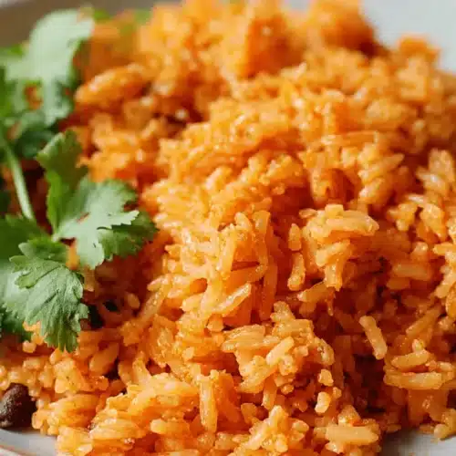Close-up of vibrant orange-red spanish rice garnished with fresh cilantro on a light plate.