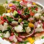 Vibrant ceviche recipe with fresh fish, red onions, and lime in a stylish gold-rimmed bowl.