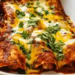 Mouth-watering beef enchiladas with red sauce, generously topped with melted cheese and fresh cilantro, served in a white baking dish.