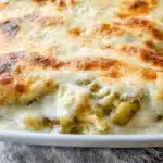 Appetizing close-up of golden-baked chicken enchiladas with white sauce in a ceramic dish.