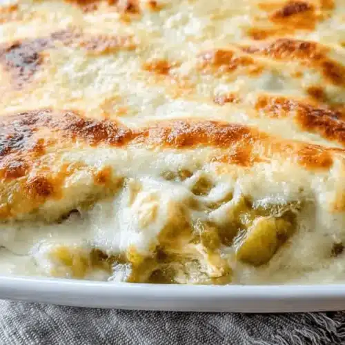 Creamy Chicken Enchiladas with White Sauce 2 Appetizing close-up of golden-baked chicken enchiladas with white sauce in a ceramic dish.