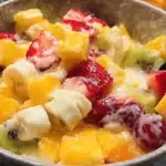 Vibrant fruit salad with vanilla pudding dressing in a decorative bowl, featuring strawberries, bananas, kiwi, and mango.