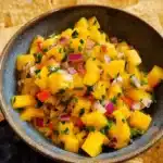 Vibrant bowl of fresh mango salsa surrounded by crispy tortilla chips.