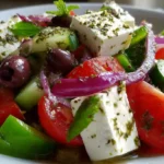 Greek salad recipe with tomatoes, cucumbers, red onion, olives, and feta cheese in a bowl.