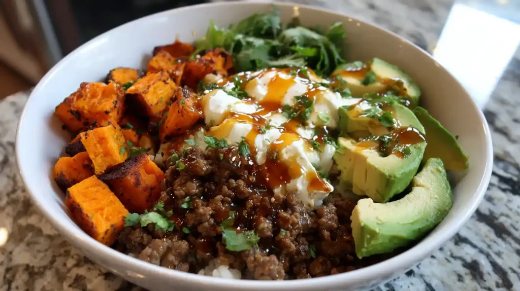 Ground beef cottage cheese bowl with avocado, roasted sweet potatoes, and rice topped with sauce and fresh herbs.