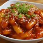 Tteokbokki recipe with spicy Korean rice cakes coated in gochujang sauce and topped with sesame seeds and green onions.
