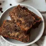 Overhead view of moist homemade Coffee Banana Bread with chocolate chips, presented as slices and a whole loaf, alongside a ripe banana and scattered chocolate chips on a linen cloth.
