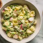 A vibrant Lemon-Dijon Asparagus Macaroni Salad in a ceramic bowl, garnished with fresh dill on a marble surface.