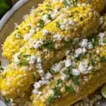 Appetizing elote recipe featuring grilled corn on the cob with cotija cheese, chili powder, and fresh lime.