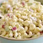 Creamy macaroni salad recipe served in a rustic bowl with red onions, celery, and black pepper.