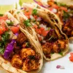 Close-up of vibrant tofu tacos with fresh pico de gallo and purple cabbage on a white plate.