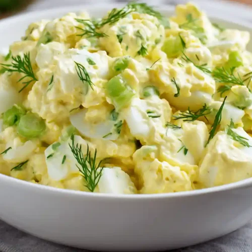 The Best Creamy Egg Salad Recipe 2 Creamy egg salad recipe with chopped boiled eggs, celery, and fresh dill in a white bowl