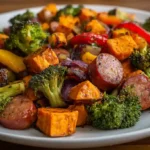 Close-up top-down view of a delicious roasted sausage sweet potato sheet pan dinner with broccoli and red bell pepper.